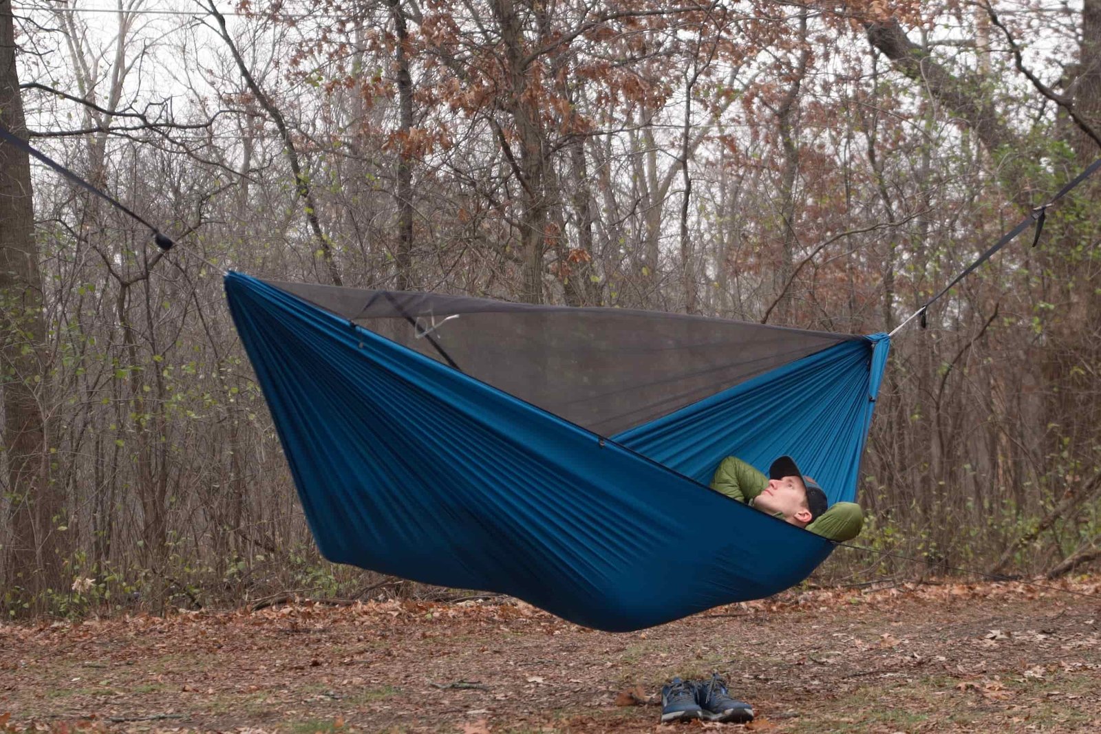 a man lays in a blue hammock in a clearing in the forest