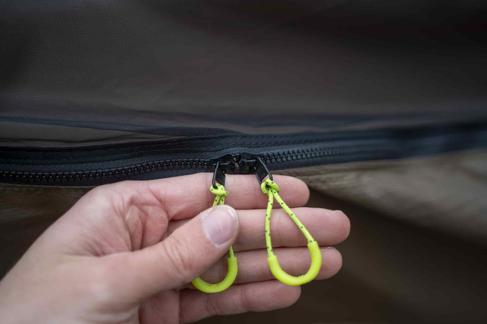 a hand holds two green loop zipper pulls