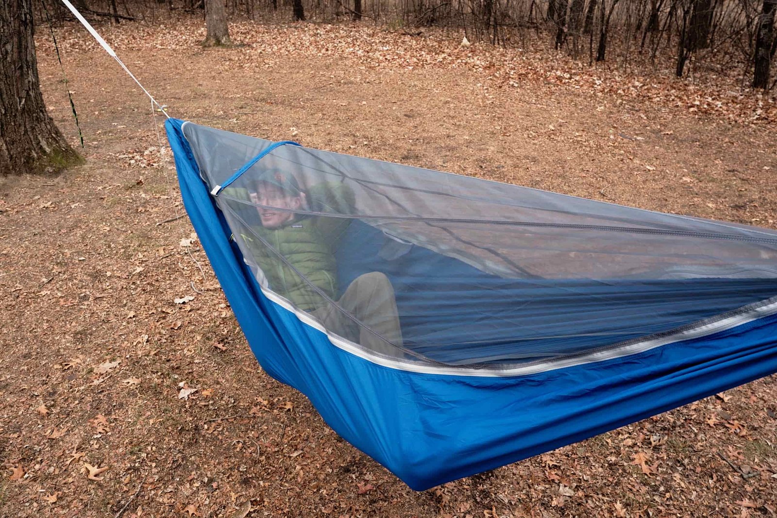 a man reclines in a blue hammock with a bug net