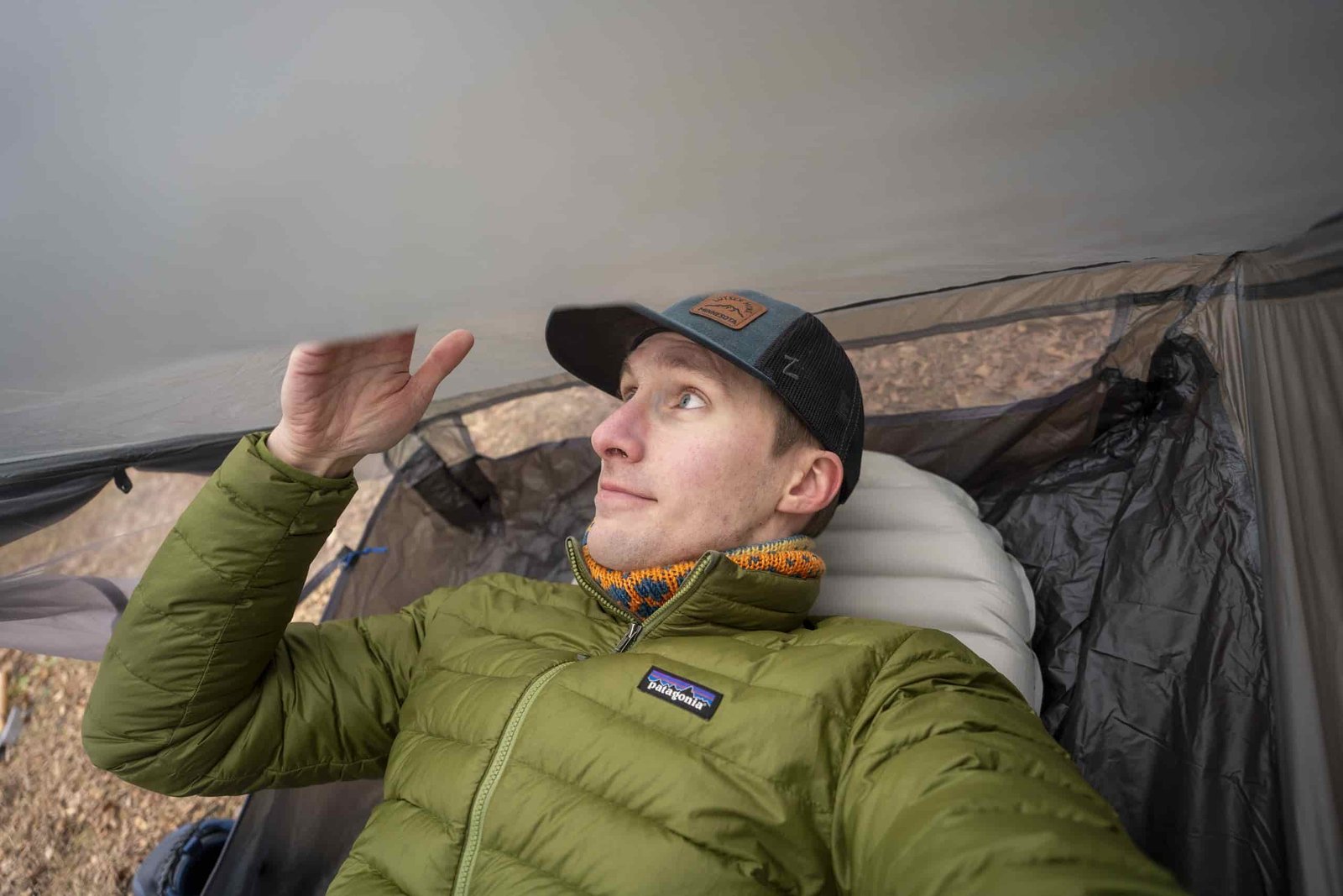 a man in a green coat touches the side wall of a tent he's lying in