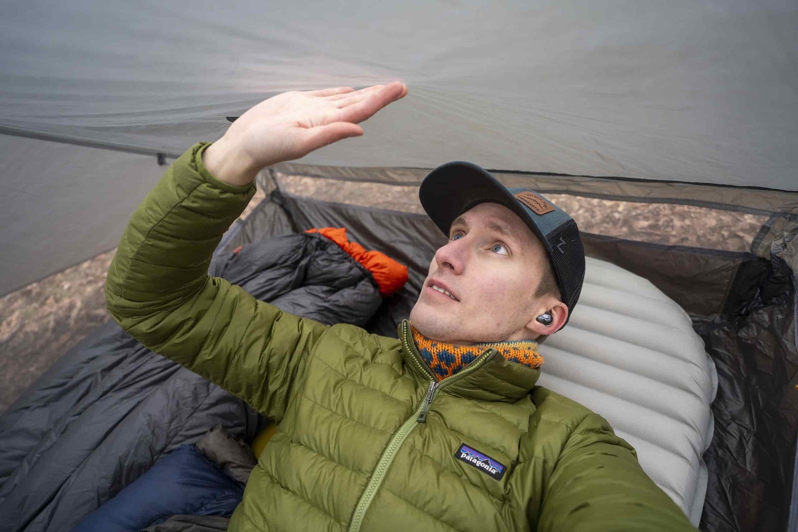 a man in a green coat lays in a tent and touches the side wall