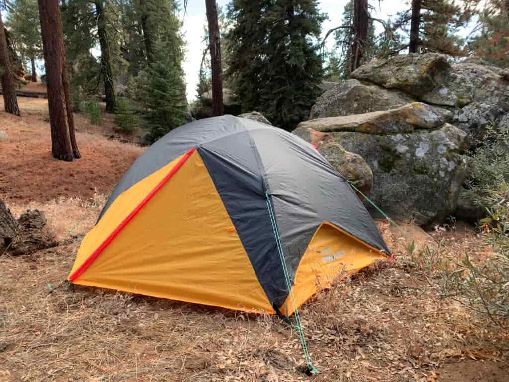 The Coleman Peak 1 fully zipped up with guy lines deployed next to a large rock with surrounding forest.