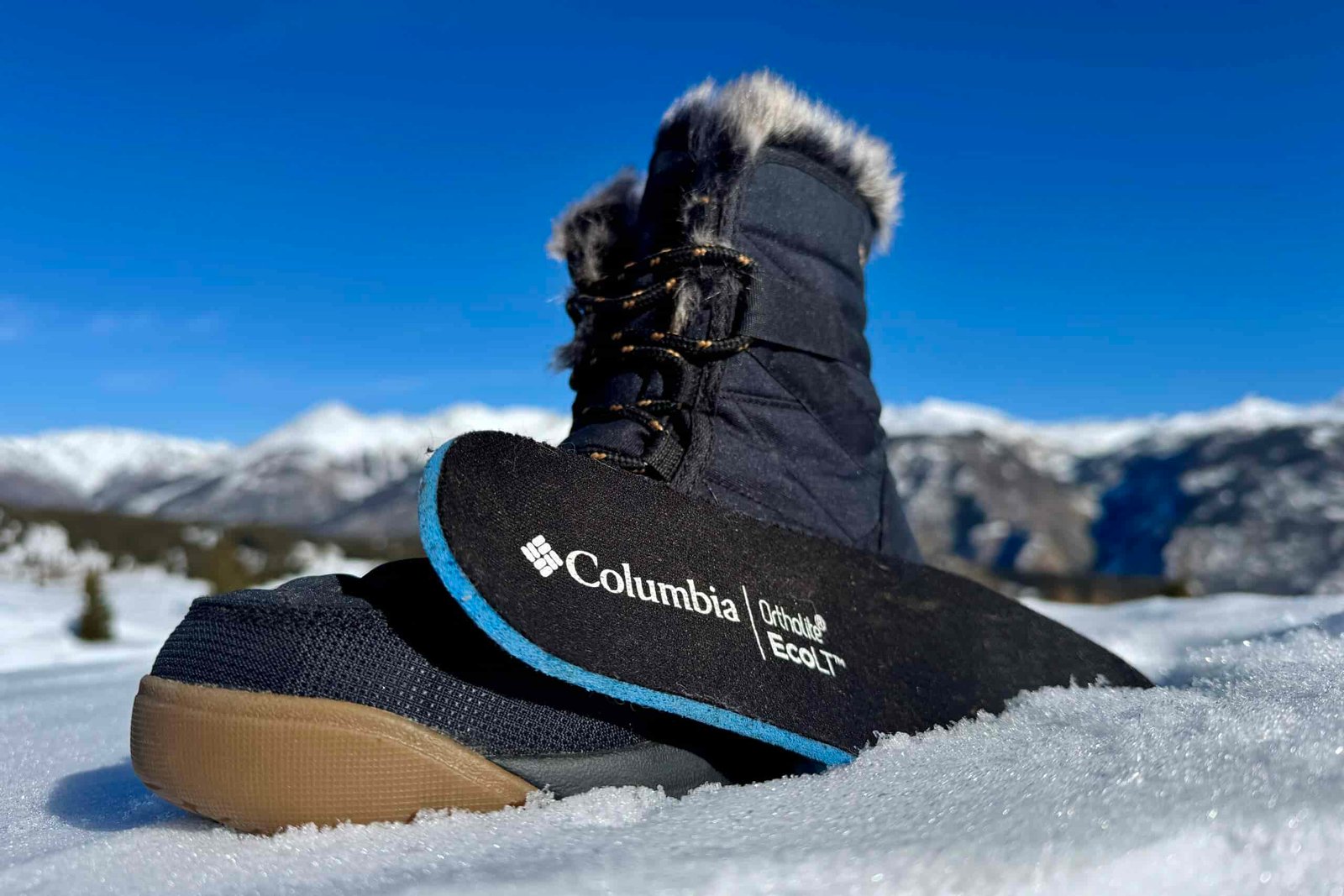 A close up of the Minx Shorty boot with the insole sitting next to it. They are set on some snow in the mountains.