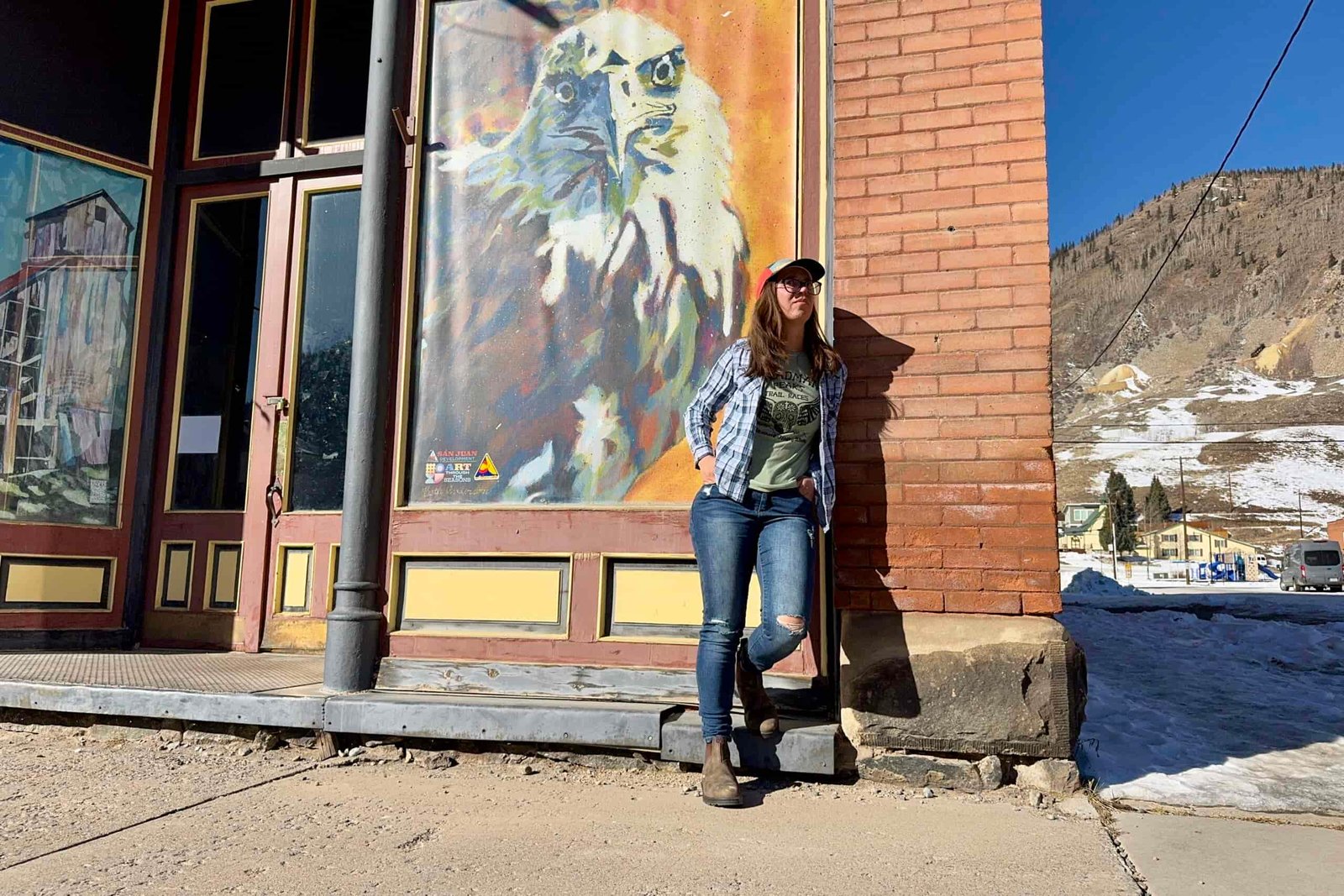 A person wearing the Blundstone Thermal Chelsea boots leans against a wall with a painting of an Eagle in a mountain town.