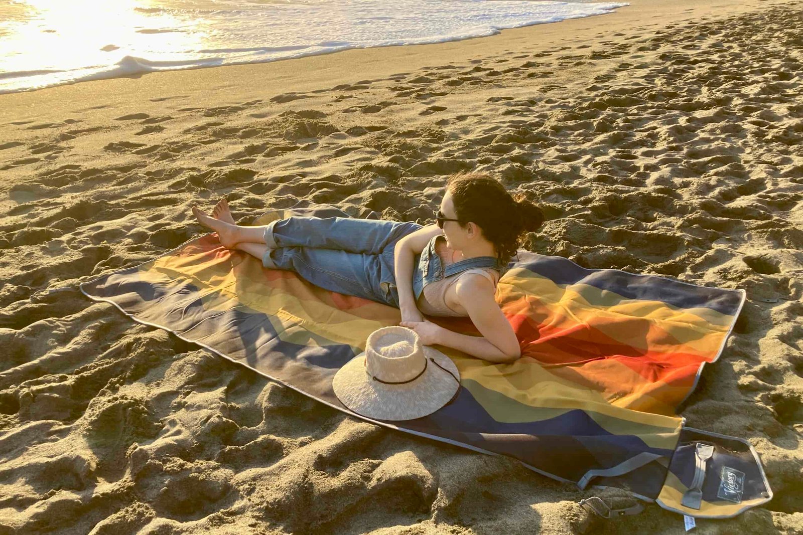 Woman laying out on the Nemo Victory Patio Blanket on the beach, gazing out at the ocean waves.