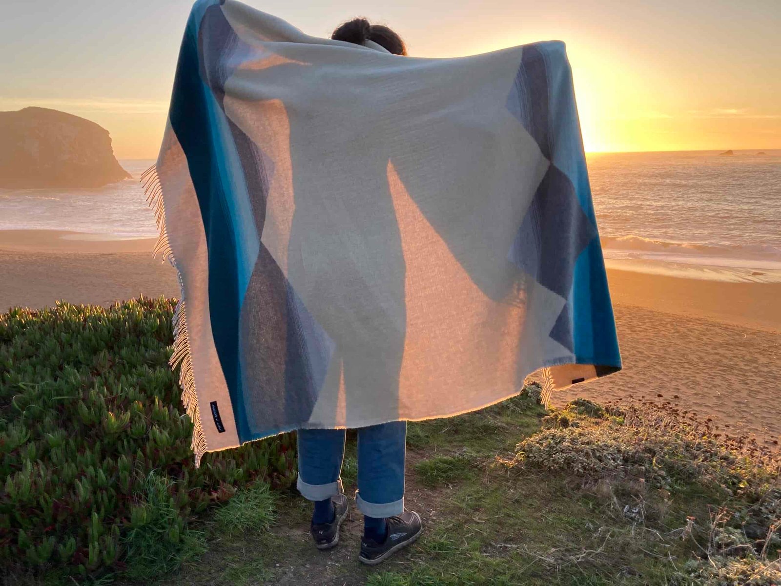 Women standing at the beach holding up the Sackcloth and Ashes blanket as she prepares to wrap herself in it