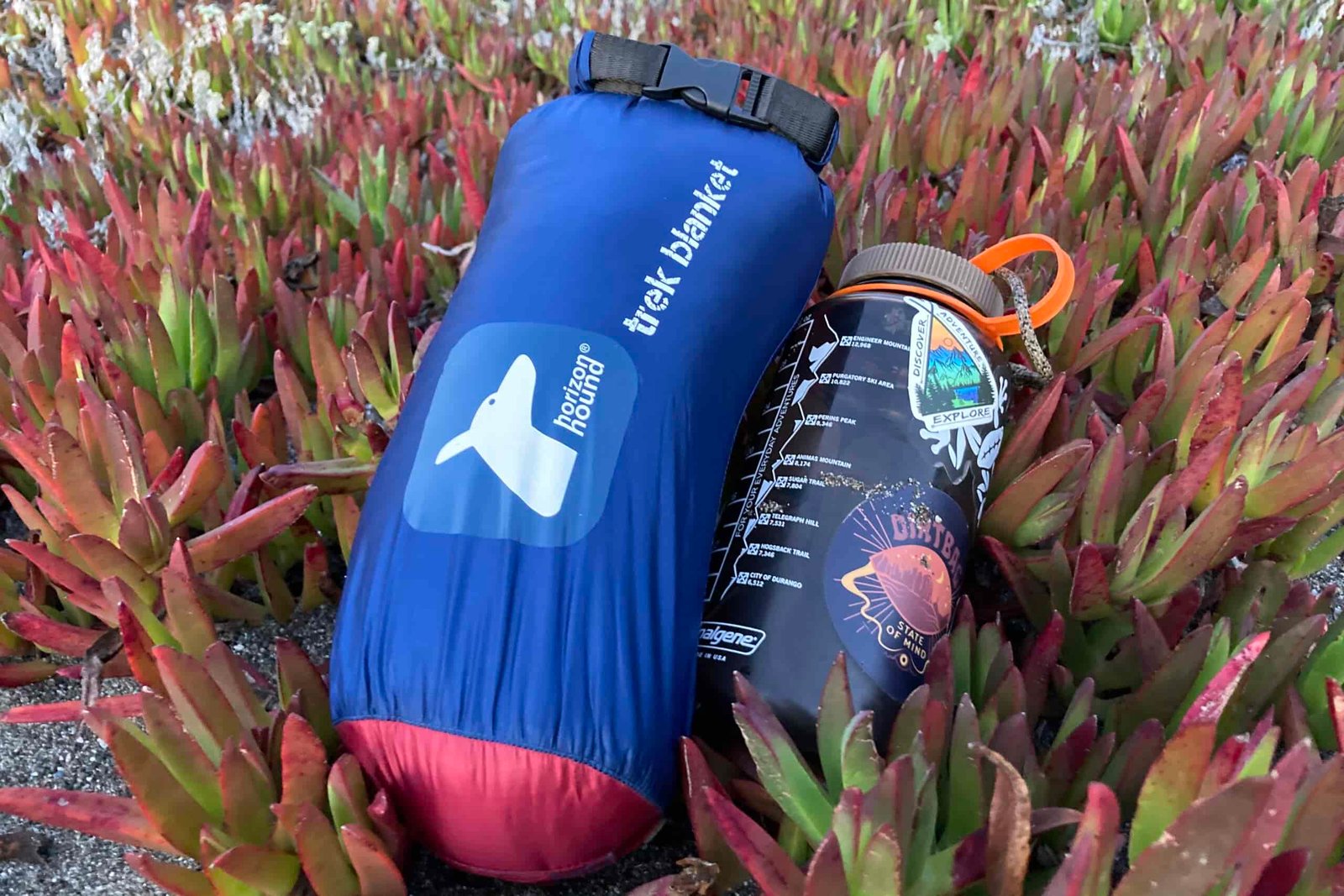 Laying the Horizon Hound Trek Blanket in its carry bag next to a Nalgene to show the relative size difference and packability of the blanket