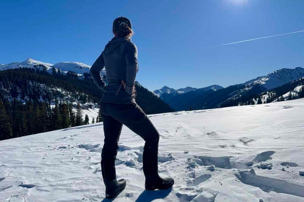 A person observing a mountain view while wearing the Neo Classic Tall boots in the snow.