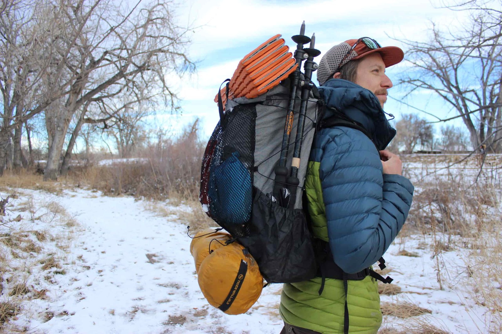 A profile view of a hiker wearing the Zpacks Arc haul ultra with trekking poles, a sleeping pad, and tent packed on the outside.