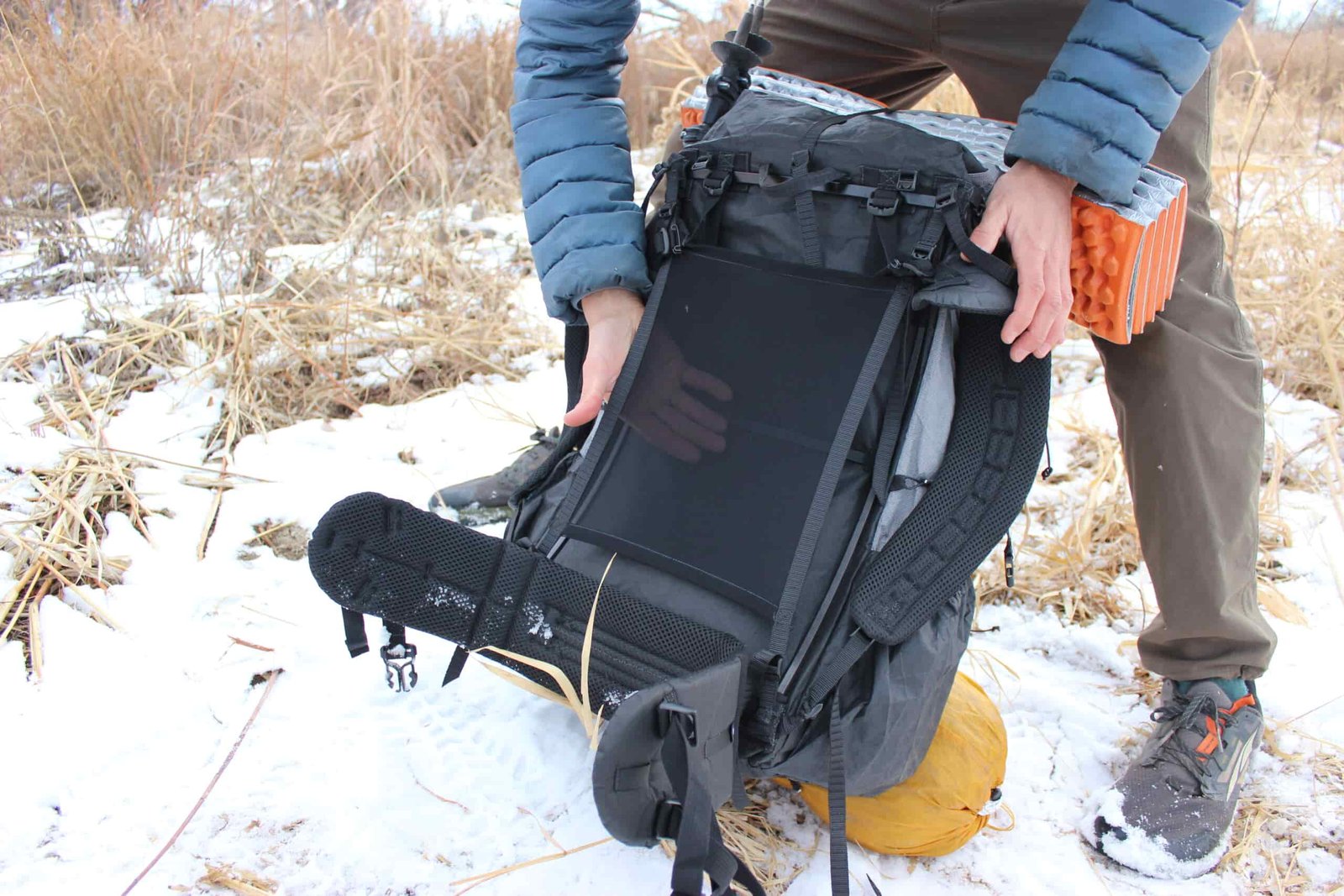 A hiker puts his hand behind the mesh on the back panel of the Zpacks arc haul ultra with snow and grass in the background.