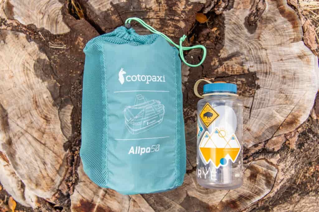 The Cotopaxi Allpa 50 Duffel packed into it's storage sack and placed next to a Nalgene for size reference.