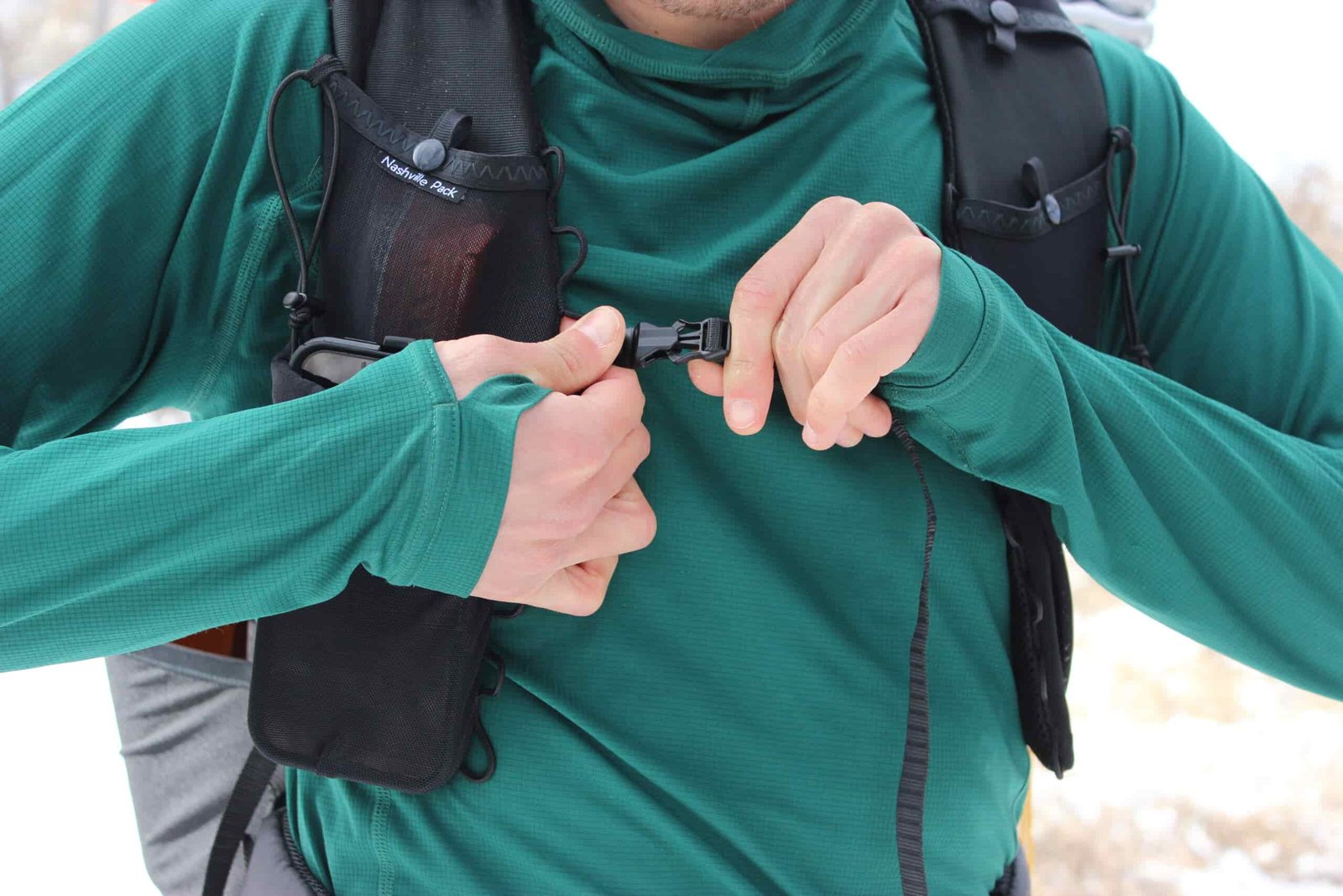 A hiker fastening the sternum strap on the Nashville Pack Cutaway while wearing a green shirt.