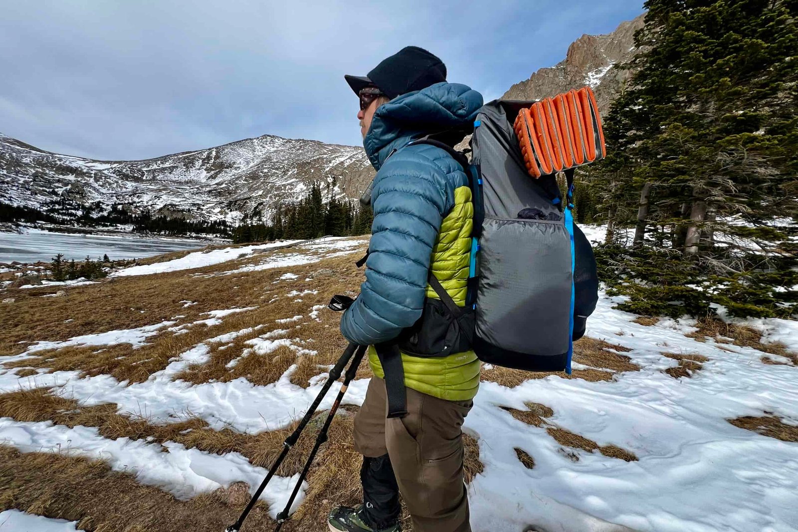 A hiker looks over a frozen lake while wearing a fully packed Mariposa 60 pack. Snowy mountains are in the background.