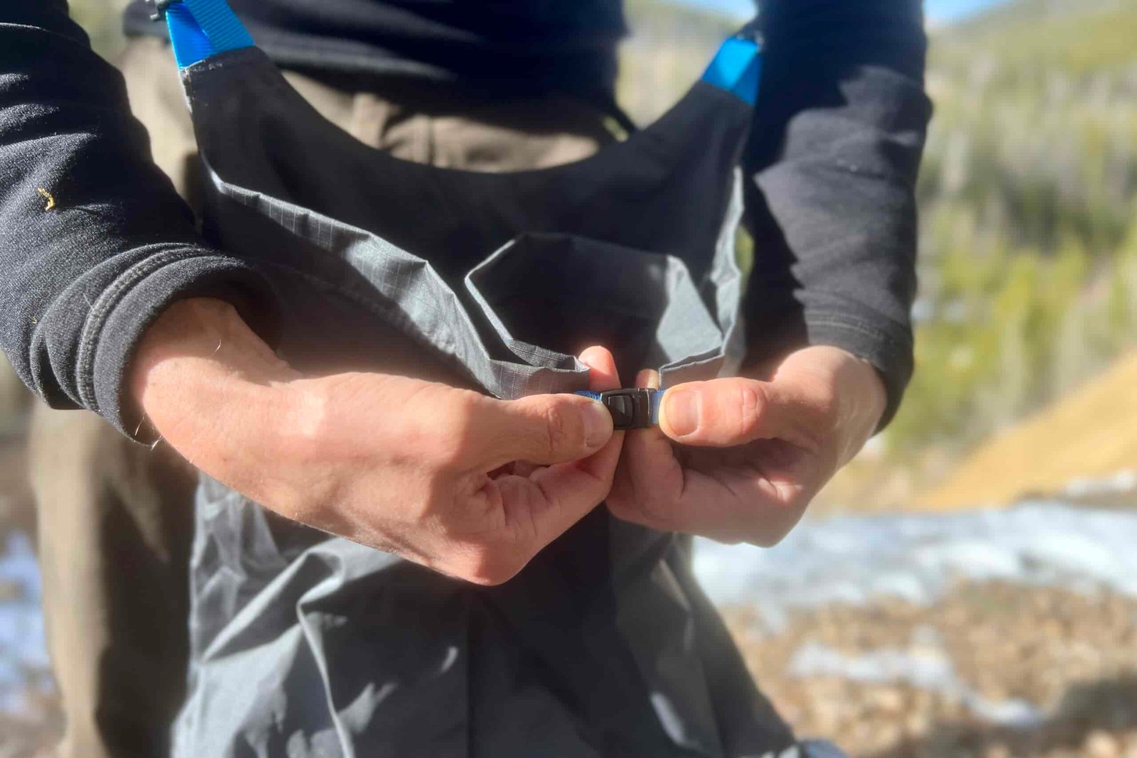 A hiker shows the buckle for the fold top closure on the Mariposa 60 with a snowy forest background.