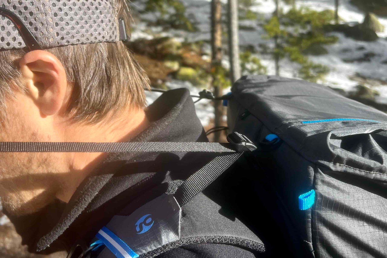 A close up of a hiker pulling the load straps on a grey backpack with a snow forest in the background.