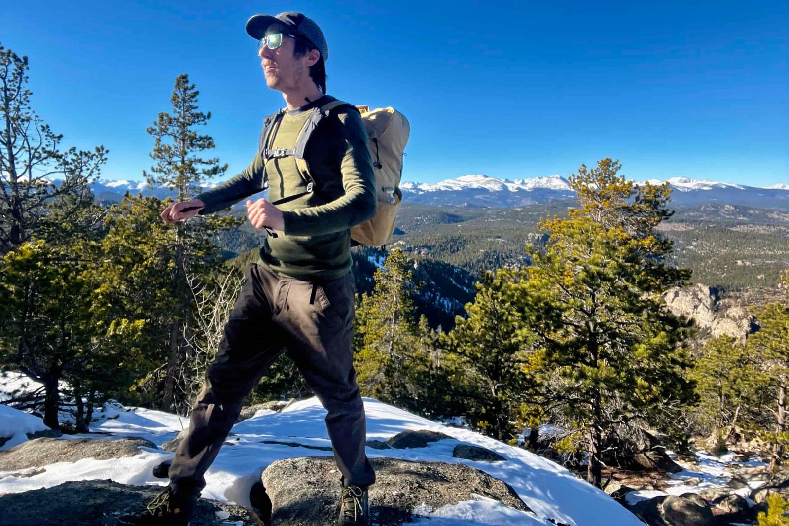A hiker tightens the straps on a backpack while wearing it and the Smartwool Intraknit. Sky, mountains, and trees in the background.