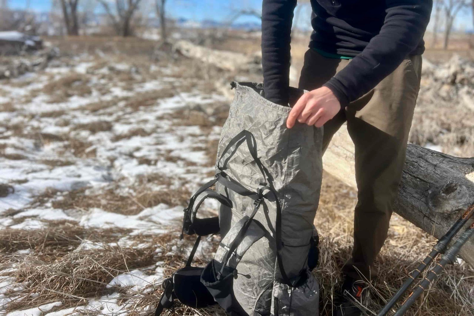 A hiker reaches into the top of a grey backpacking backpack with a winter scene in the background.