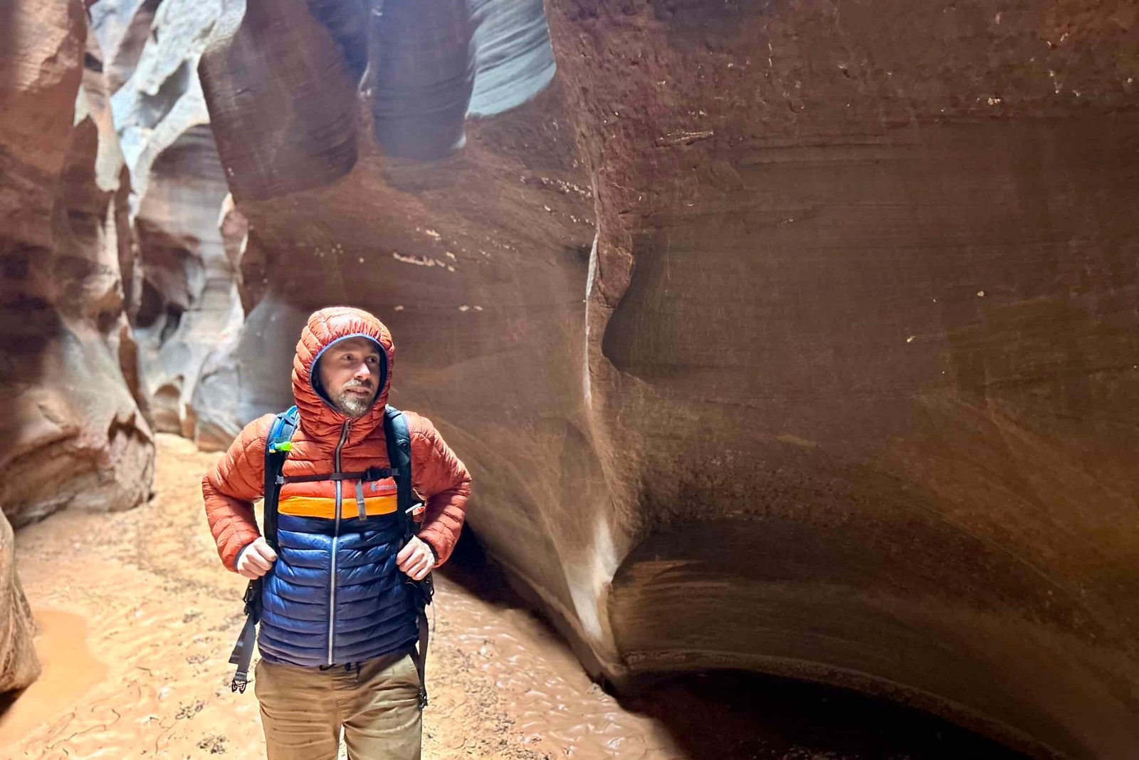 A man in a puffy jacket smiles as he walks through a desert canyon.