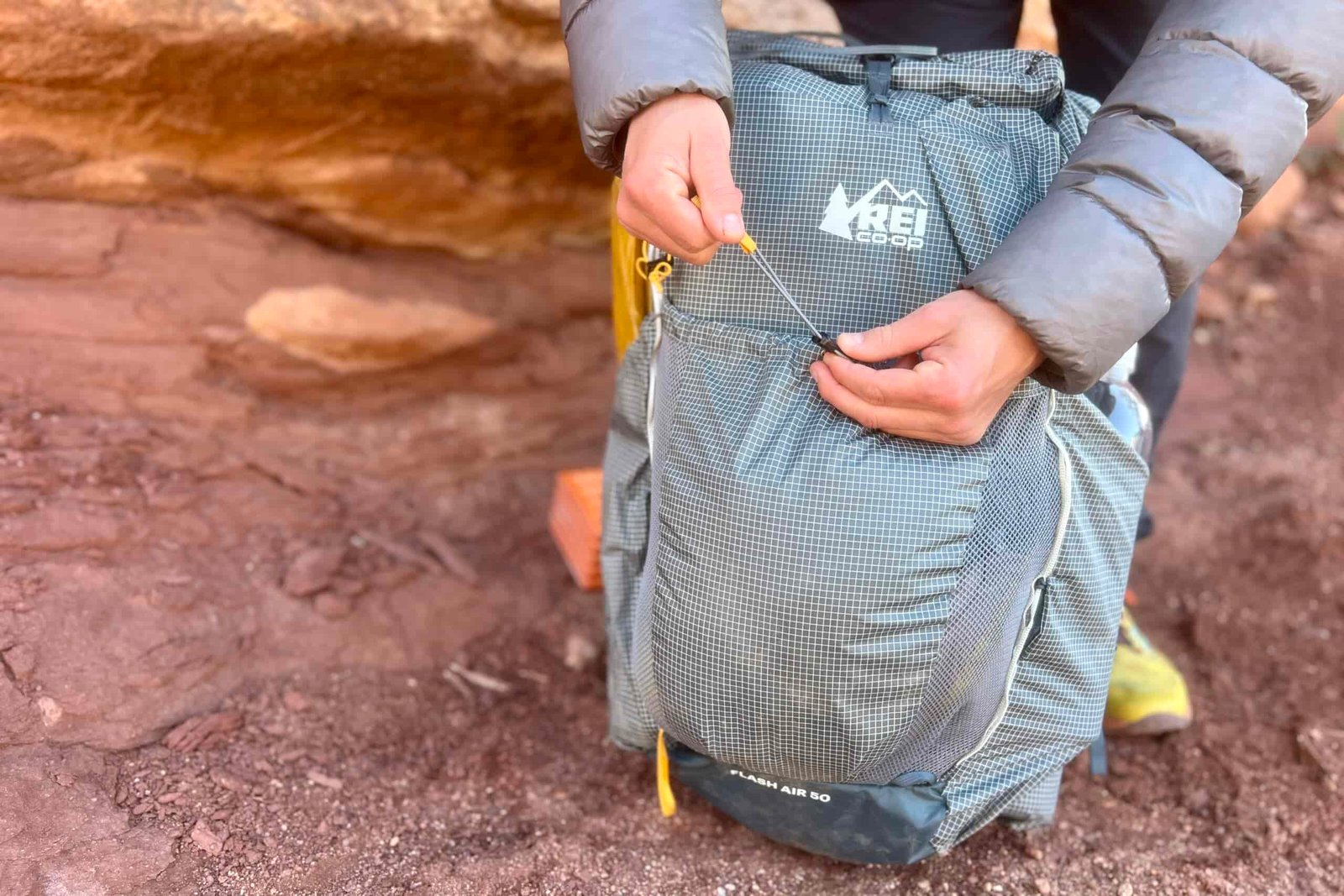 A hiker pulls on the adjustment of the front pocket on a backpack with red rocks in the background.