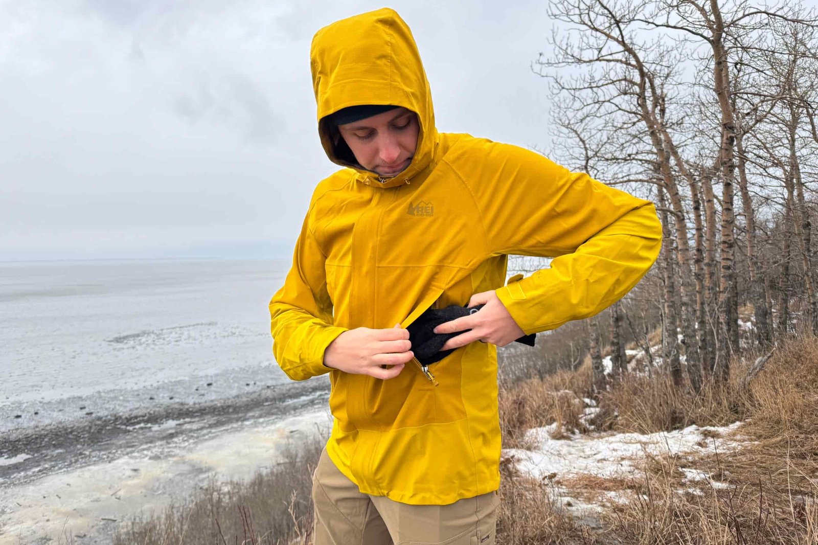 A man puts a pair of gloves in the pocket of a rain jacket.