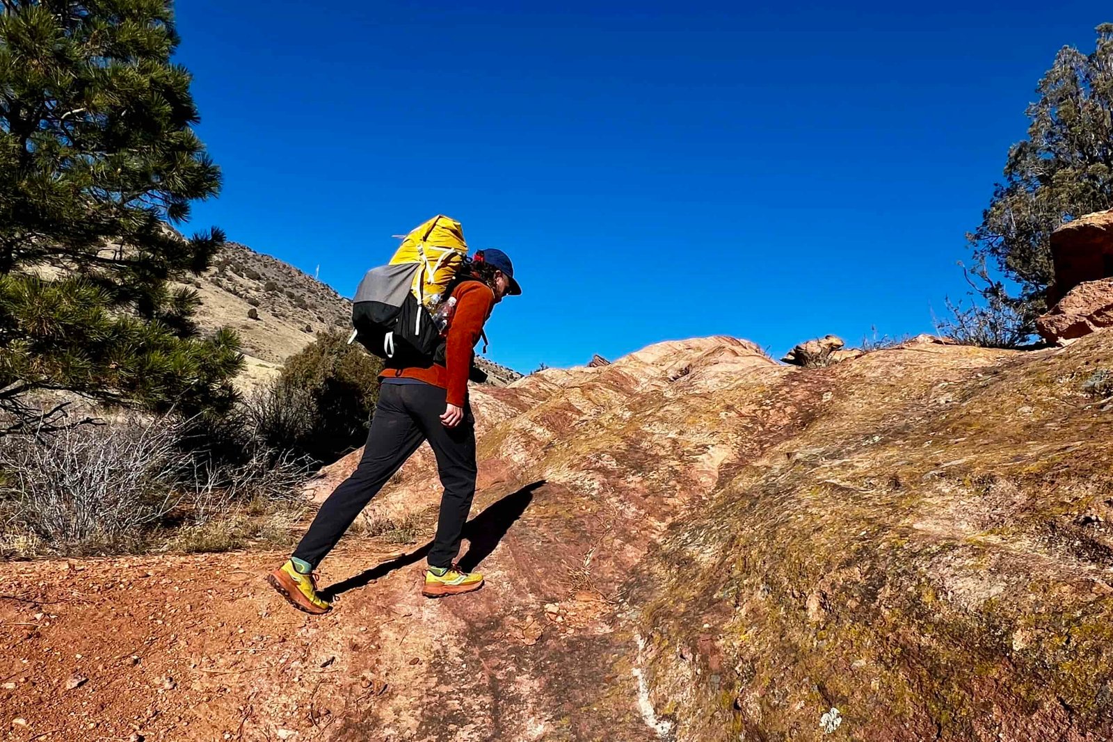 A hiker traversing red rock while wearing the Gorilla 50 backpack.