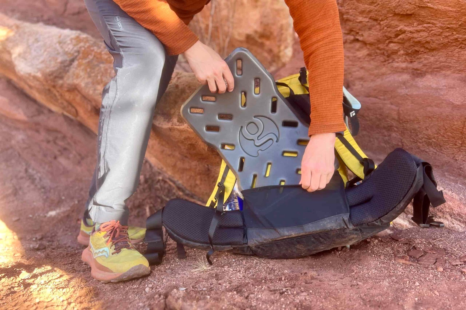 A person replacing the removable sit pad/back panel on a backpack. Red rocks in the background.