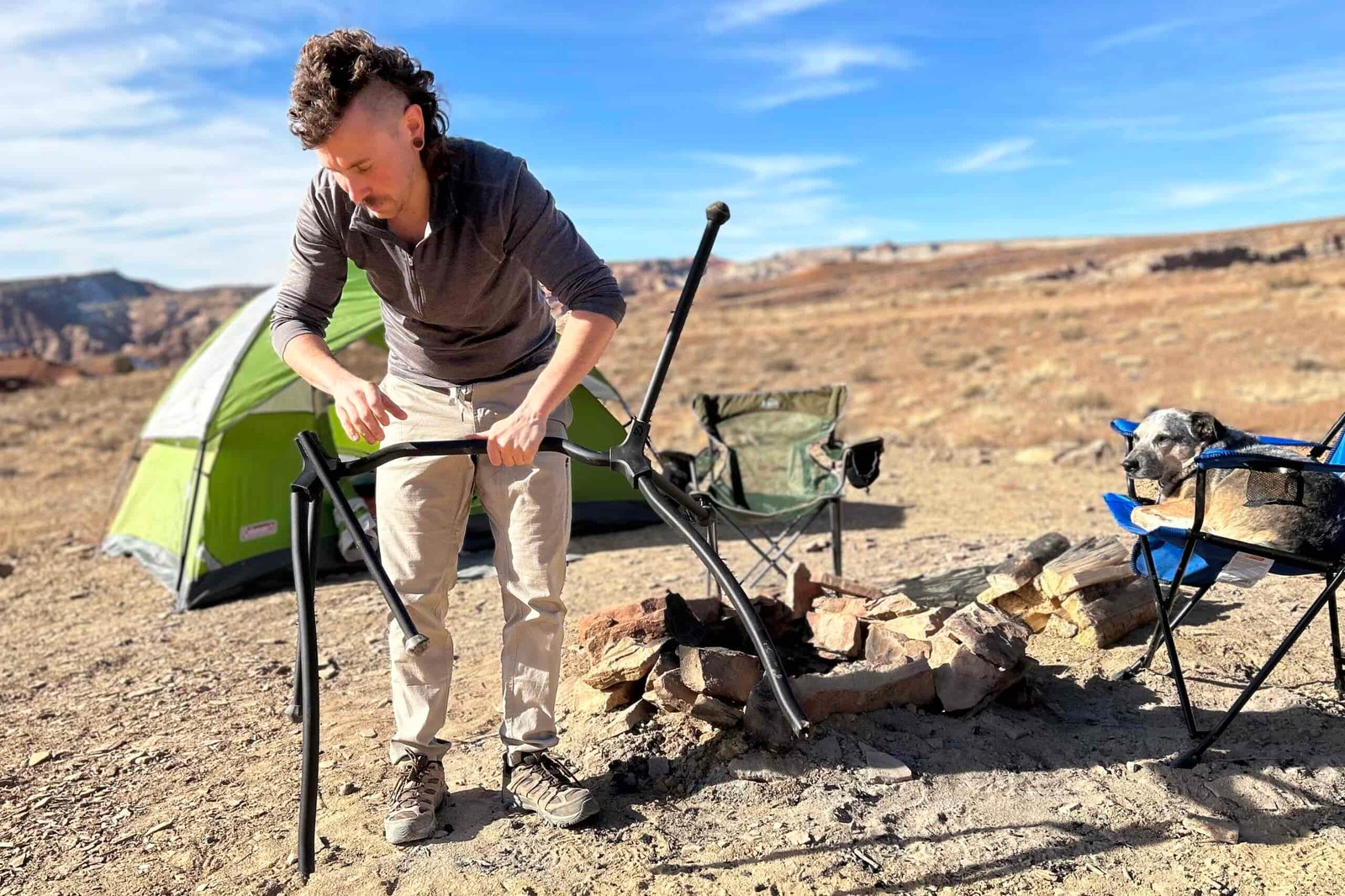 A man sets up a camping chair frame in front of a tent.