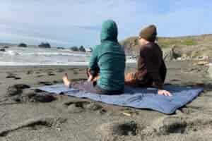 2 people sitting on the Yeti Lowlands Blanket at the beach.