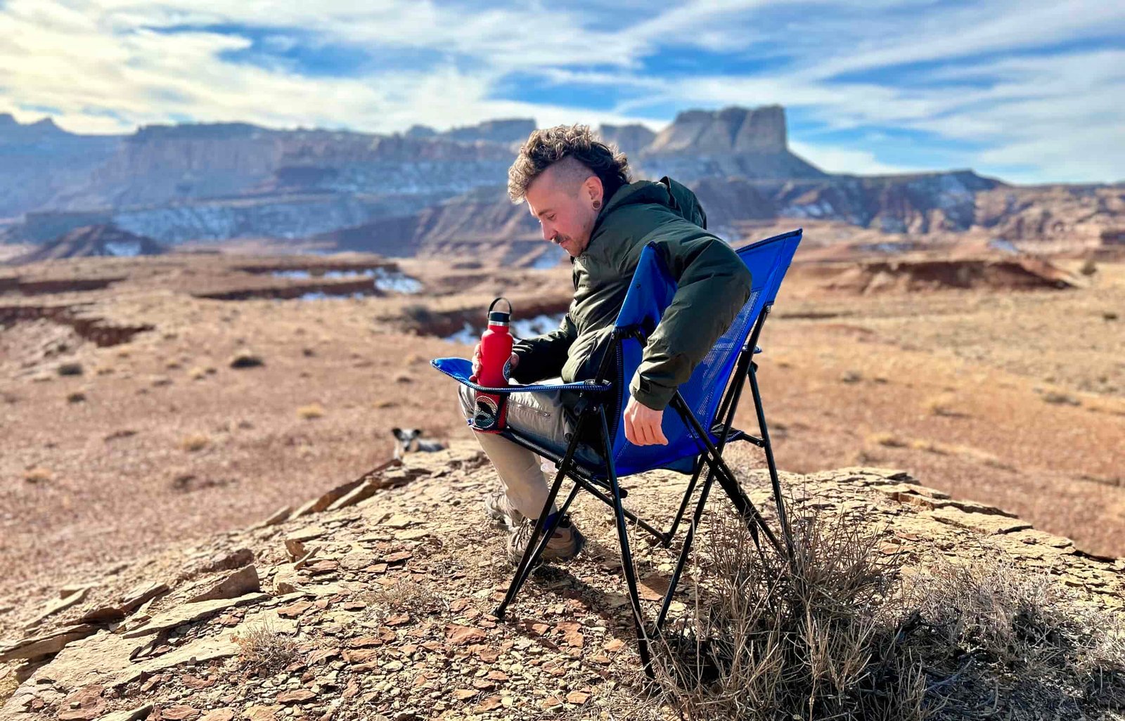 A man sits in a camping chair in a sunny desert setting.