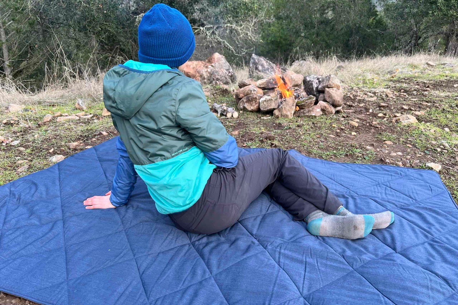 Women laying on her side on the Yeti Lowlands Blanket beside a small campfire.
