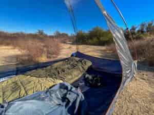 Inside view of the Kelty Late Start 2 interior showing the mesh walls, bathtub floor and floor space. Dry patches of grass and scattered bushes in the background