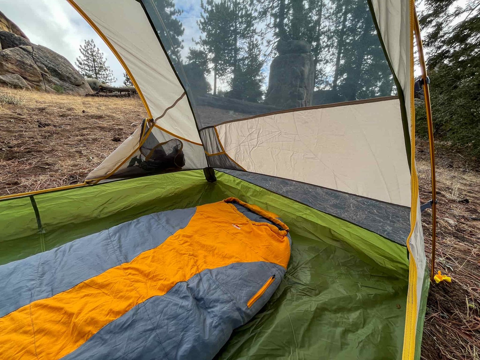 A sleeping bag rests on the floor of the Mountainsmith Morrison EVO 2 tent, with a view of trees and rocks through the mesh wall.