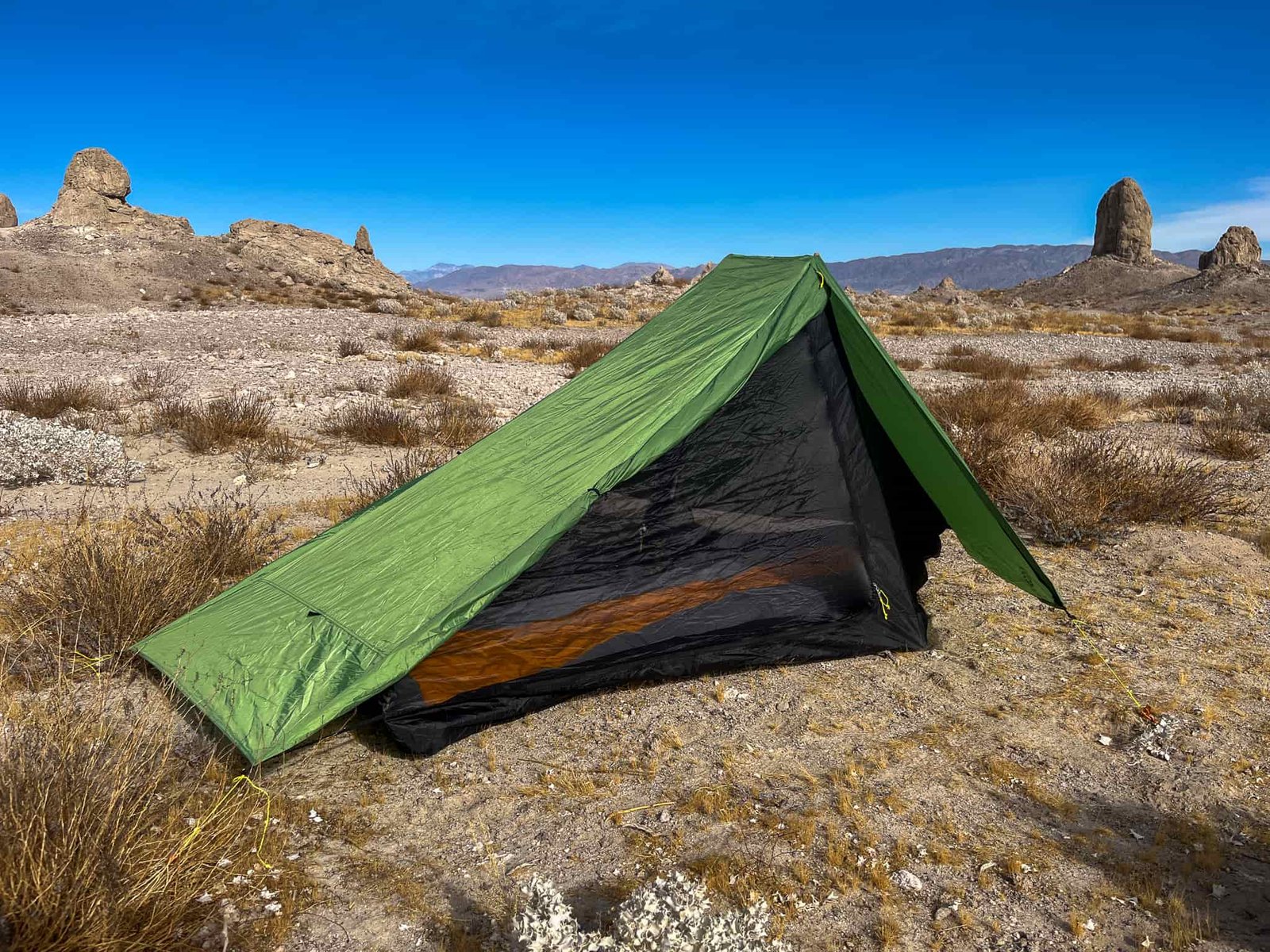 Three-quarter view of the Six Moon Designs Skyscape Scout showing one half of one vestibule rolled back revealing the inner mesh portion. Blue sky and desert landscape visible in the background.