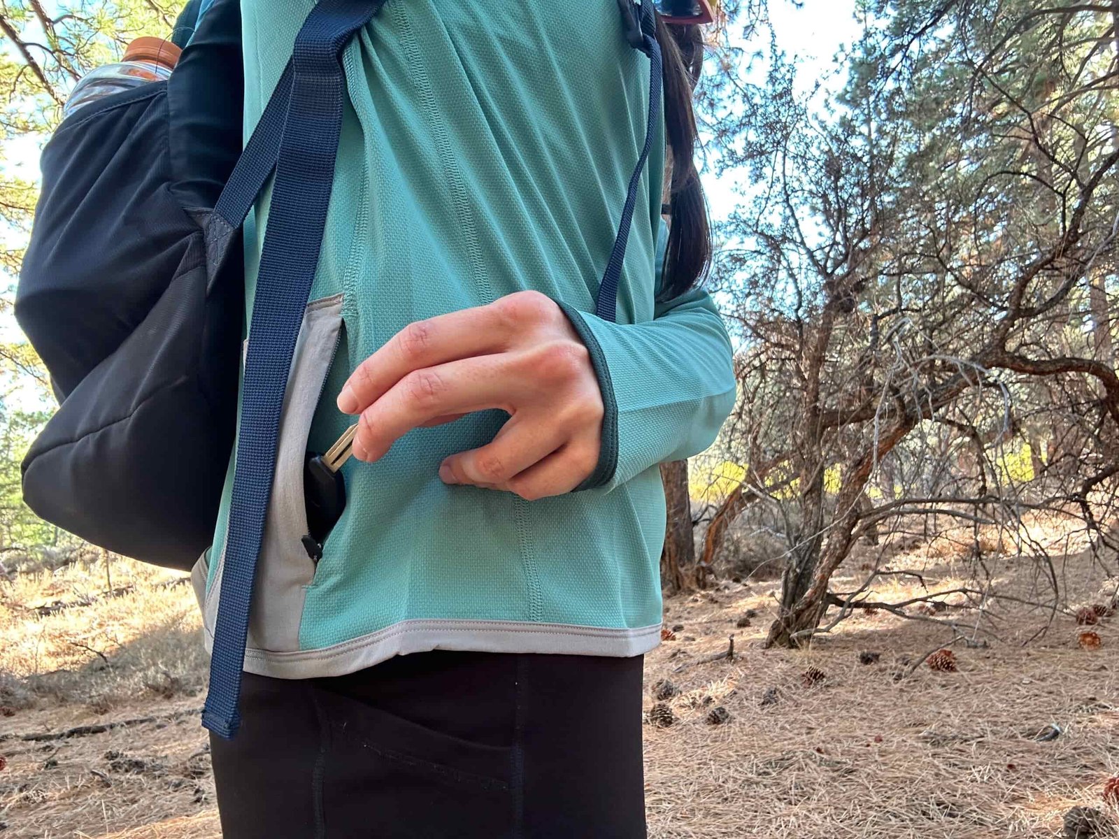 Hiker showing off the Cotopaxi Sombra Sun Hoodie's zippered pocket on the side of shirt.