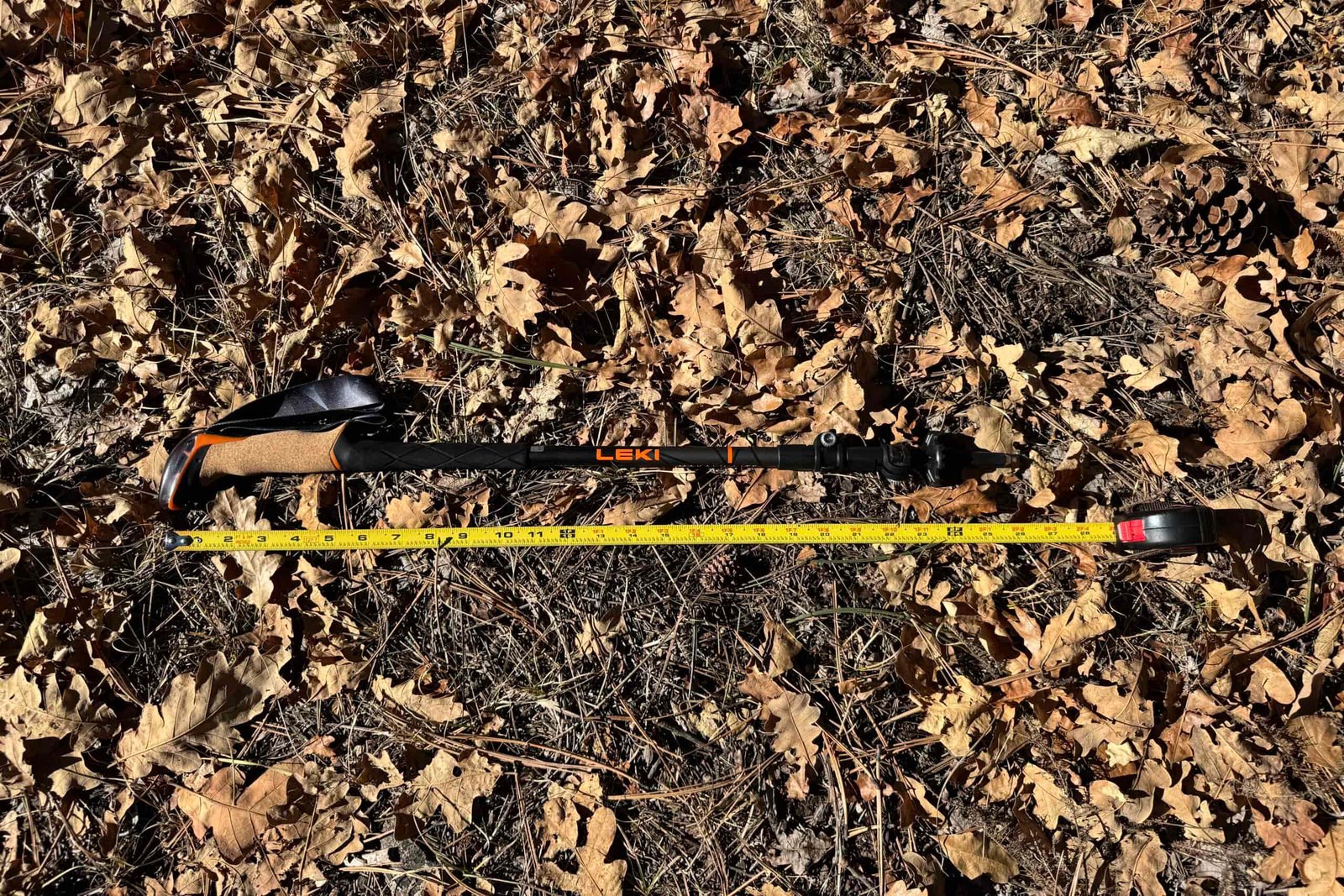 The Leki Makalu Cork Lite pole is laying on the ground in some leaves with a measuring tape next to it.