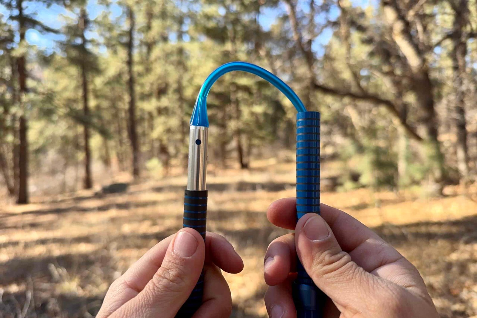 A close up of two hands holding a folding trekking pole and showing the inside cable. There is a forest in the background.