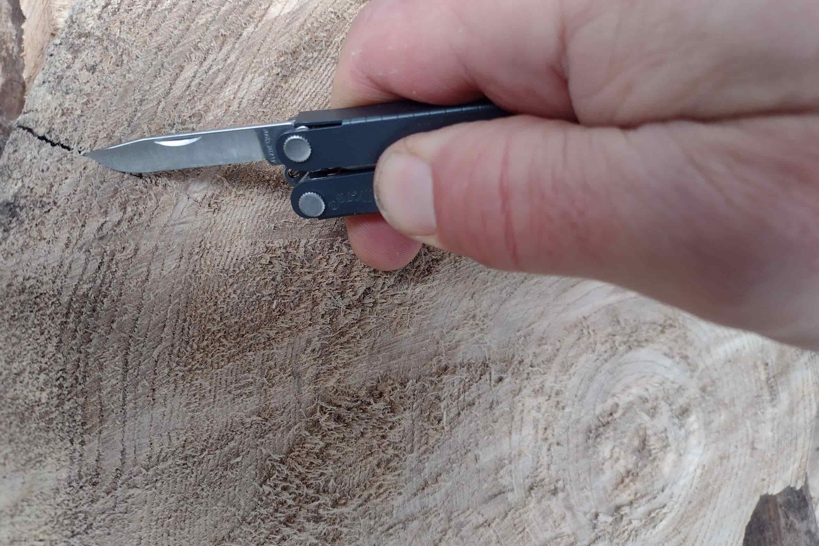 The Leatherman Micra in hand, scoring a cut on a log with its blade.