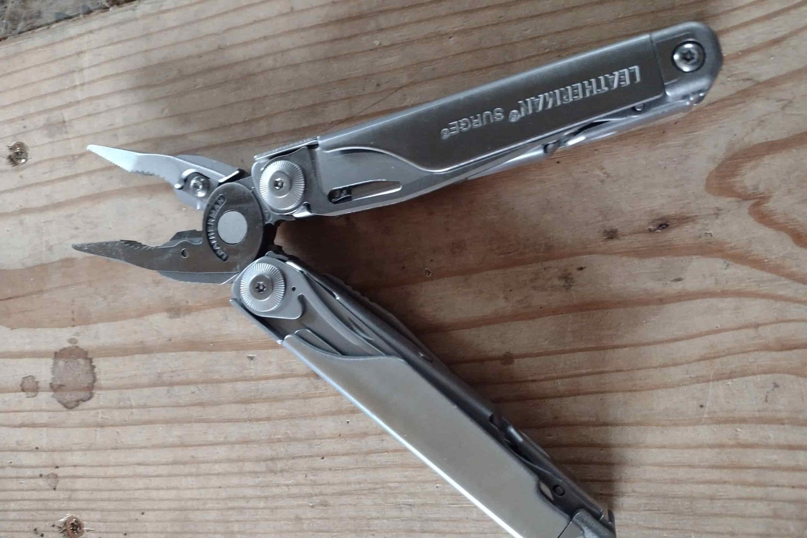 The silver Leatherman Surge resting on a board, with its handles and pliers open.