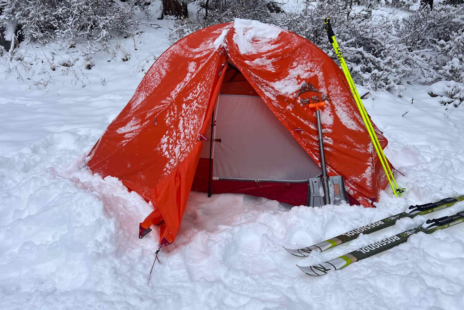 The MSR Access 2 tent pitched in snow, with skis and a snow shovel propped against the tent.