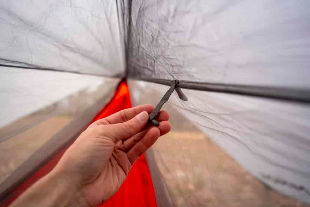 A hand holds a toggle on the interior of a hammock bug netting