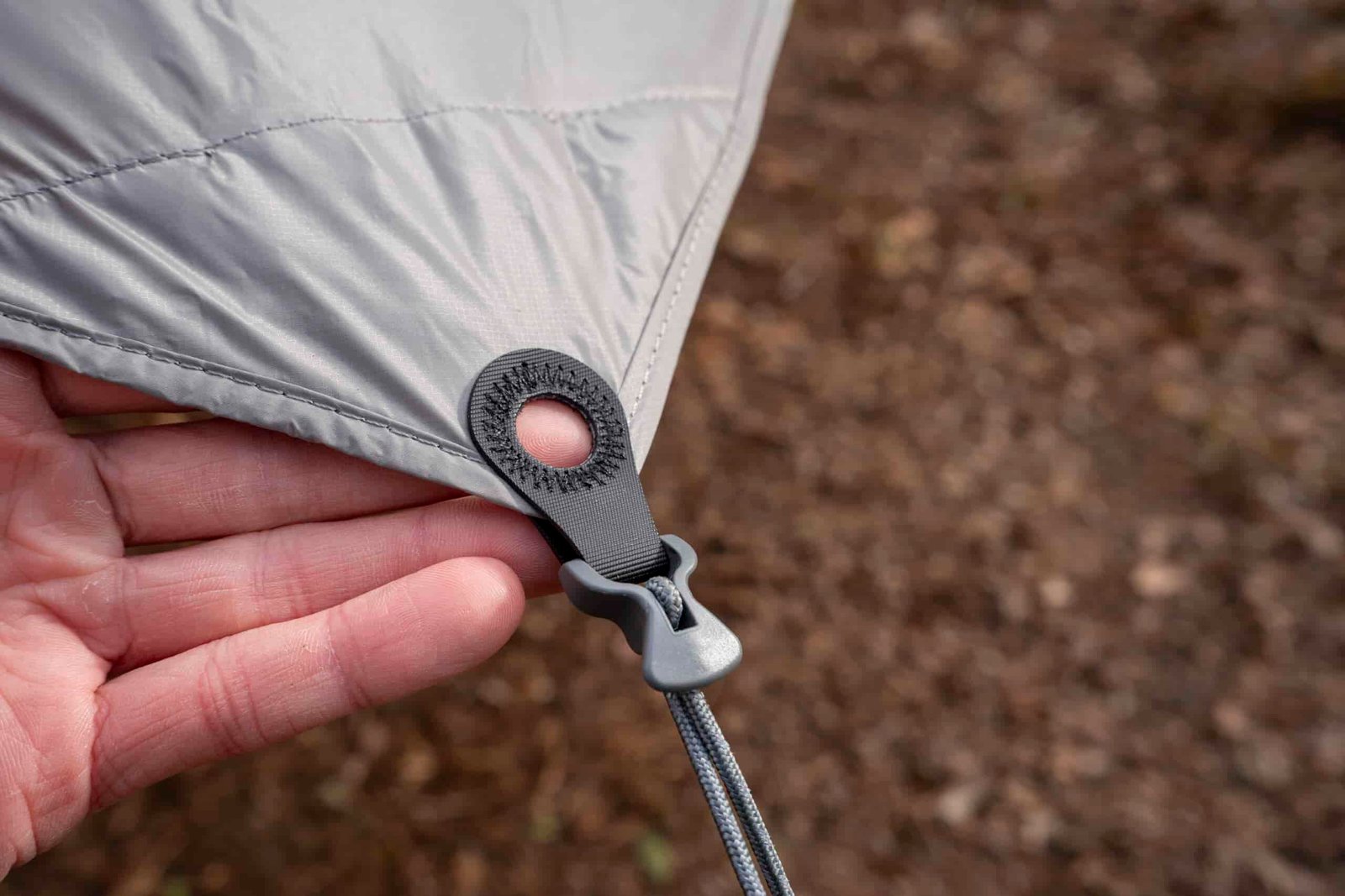 A hand points to a cord attached to a corner of a tarp