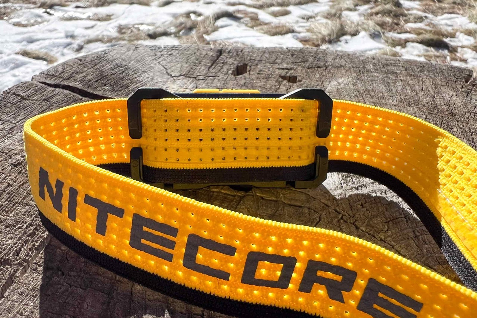 Close-up of the Nitecore NU27 headlamp strap and back attachment, showcasing its breathable, perforated design and easy-to-remove mechanism, resting on a weathered wooden surface.