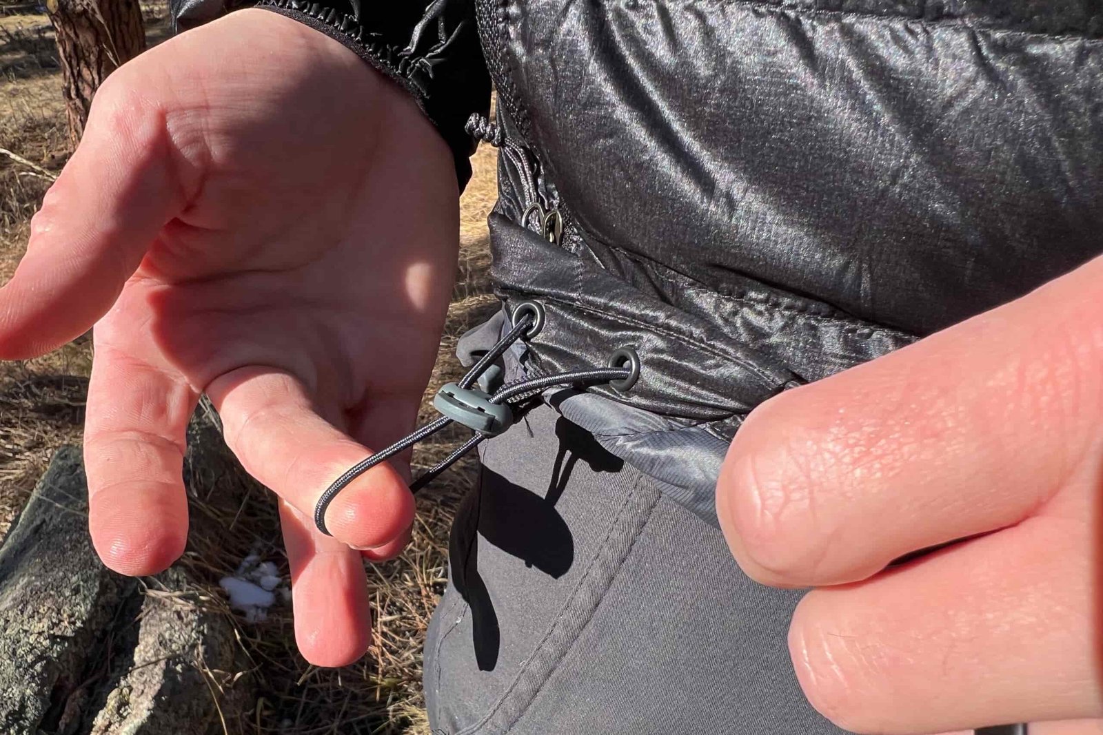 Close-up of a hand adjusting the drawcord hem on the Outdoor Research Helium Down Hoody, showing the elastic cinch system.