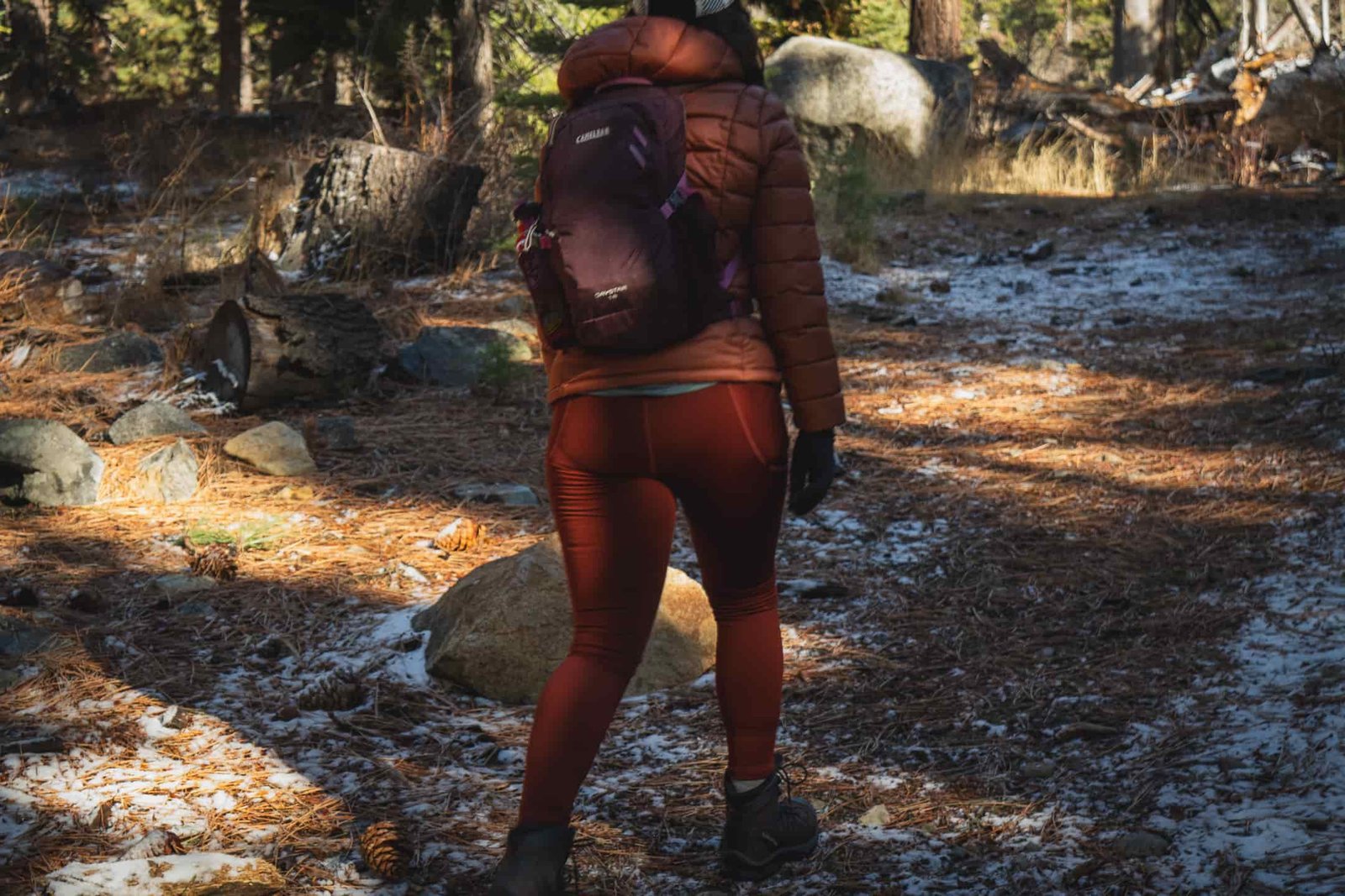 Person in reddish/orange leggings, with dry grass in background, wearing a bronze colored down jacket and black gloves