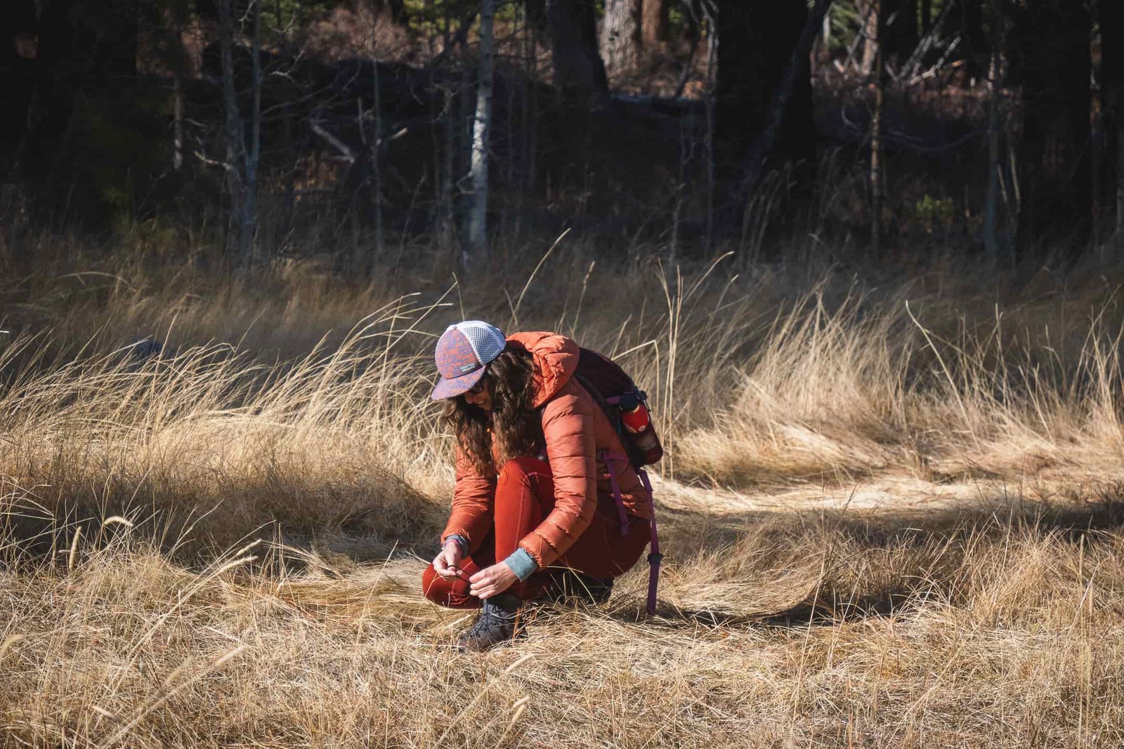 Person in reddish/orange leggings, with dry grass in background, wearing a bronze colored down jacket and black gloves