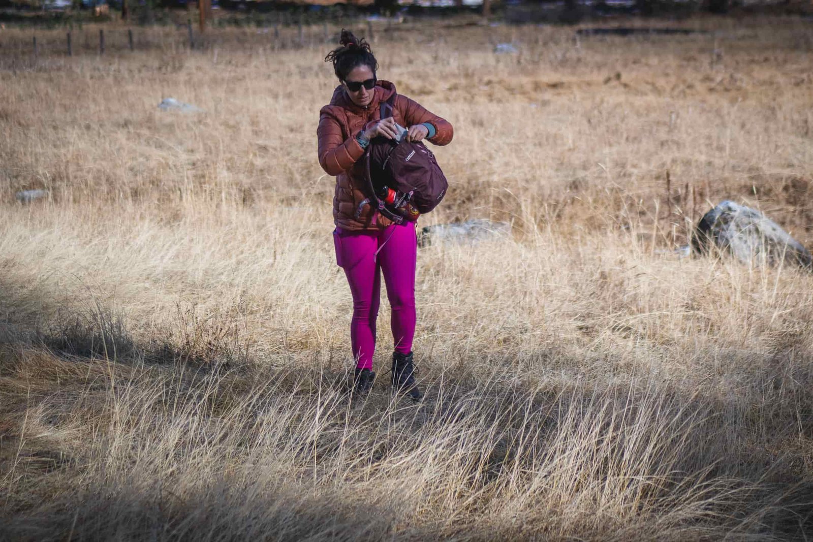 Person hiking in bright pink leggings, wearing a bronze down jacket and black gloves.