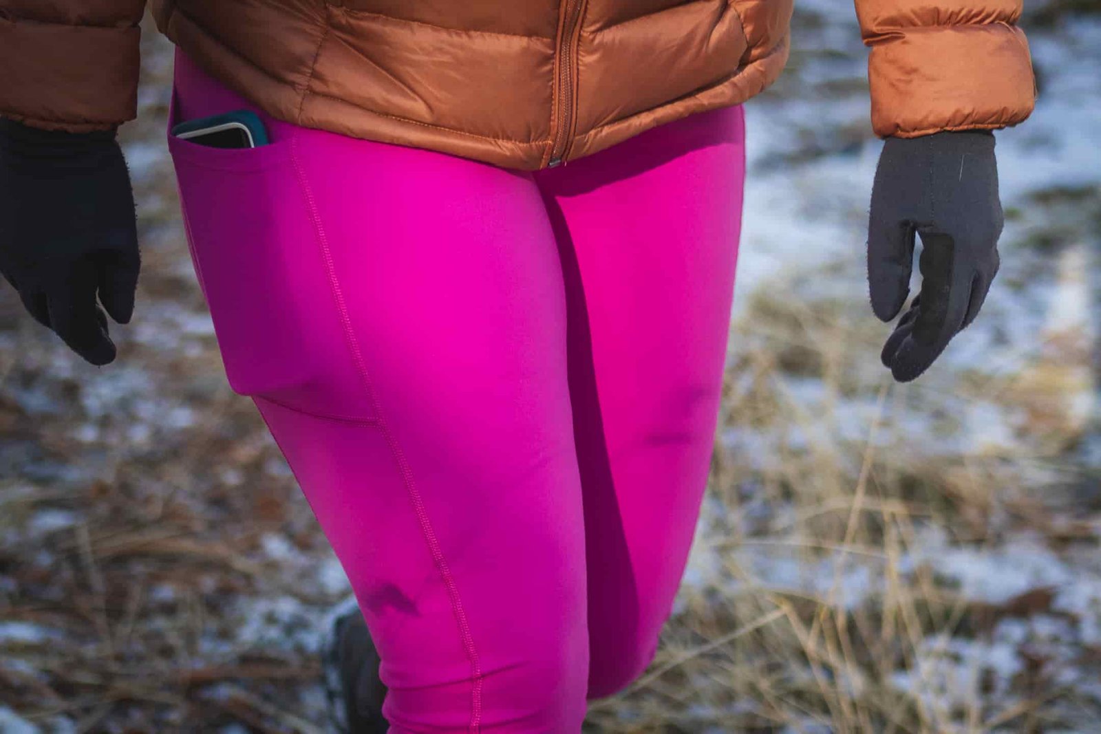 Person hiking in bright pink leggings, wearing a bronze down jacket and black gloves.