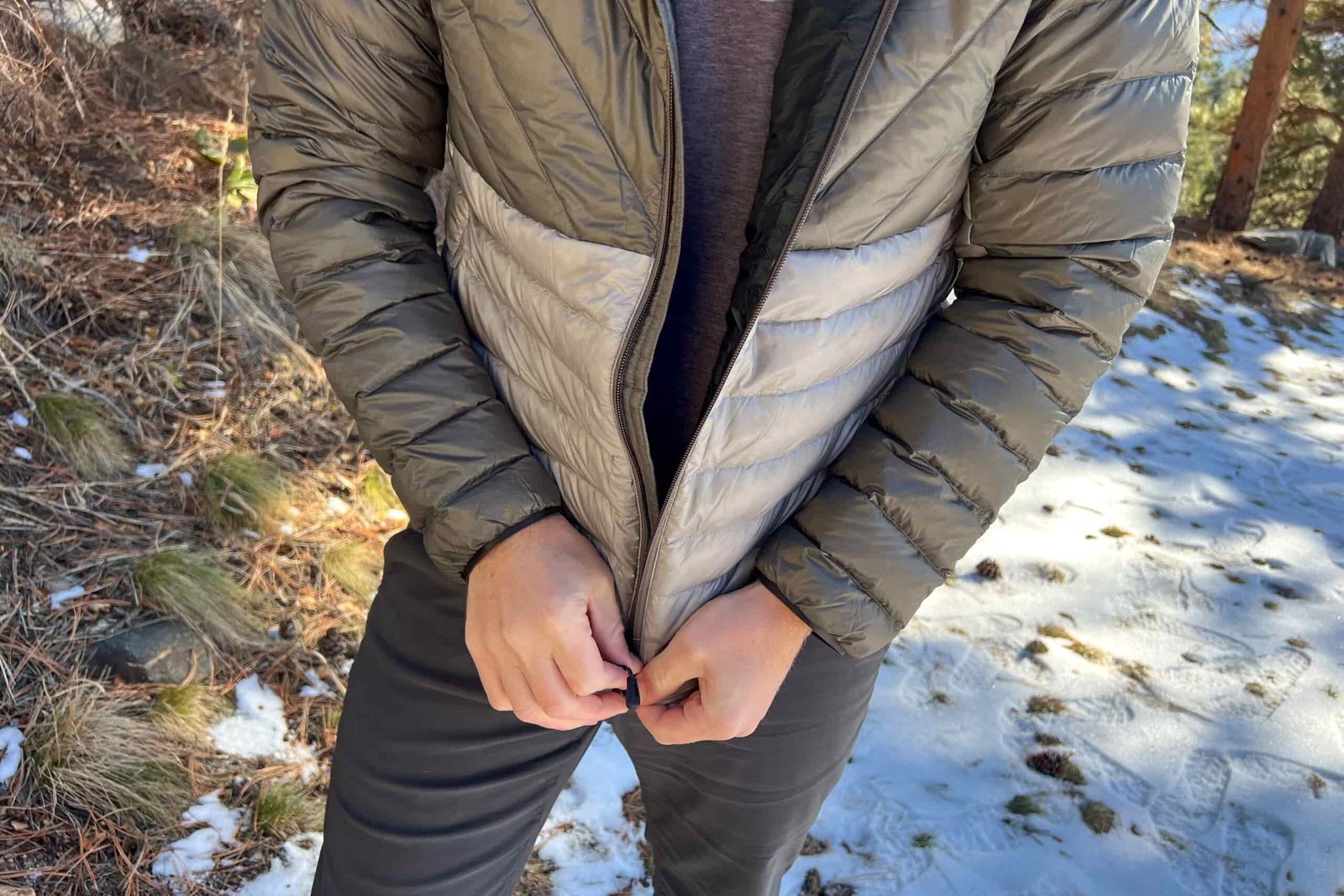 Close-up of a person zipping up the REI Magma 850 Down Hoody, showing the two-tone gray design.