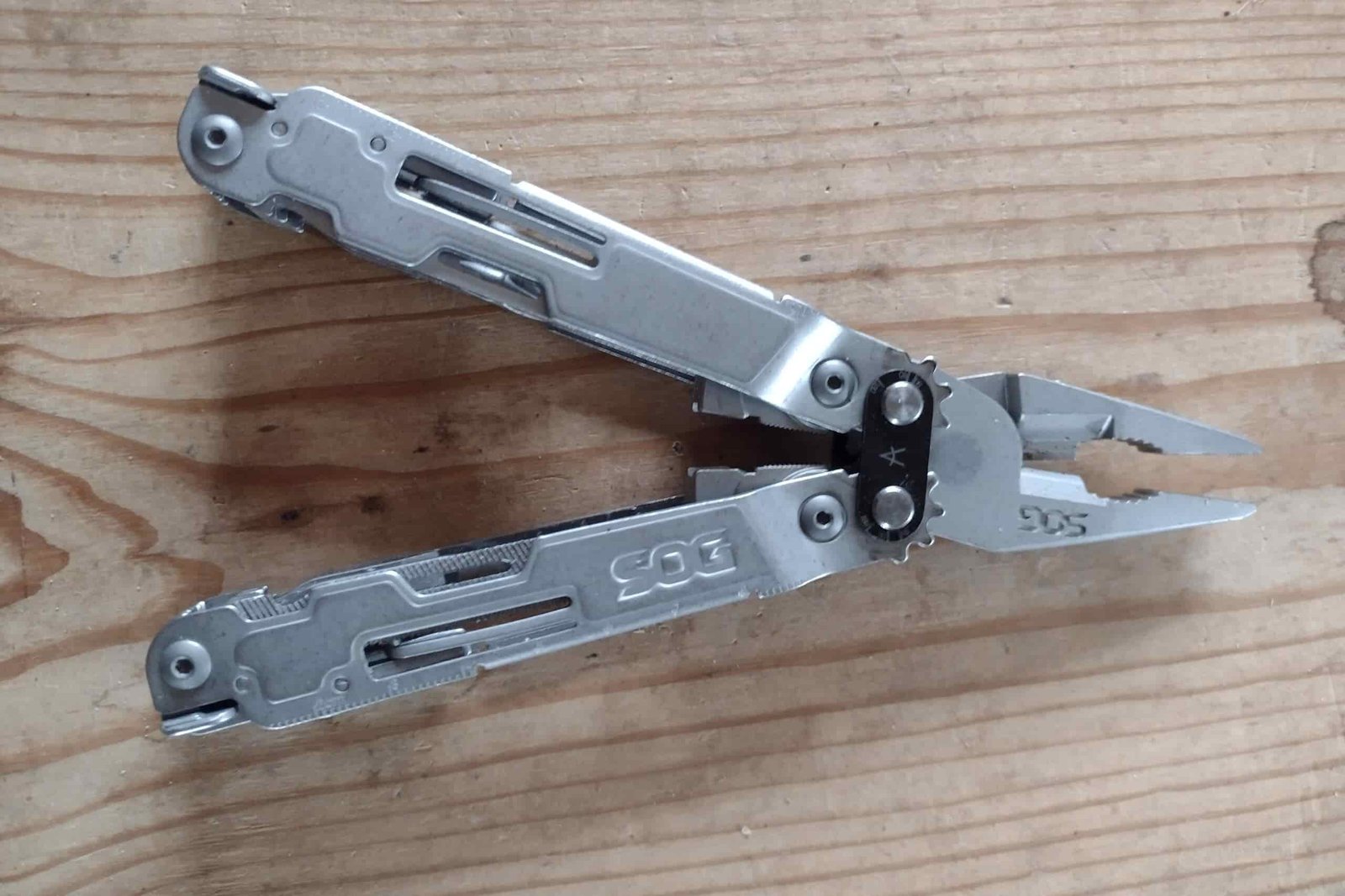 The silver SOG PowerAccess Deluxe resting on a board, with its handles and pliers open.
