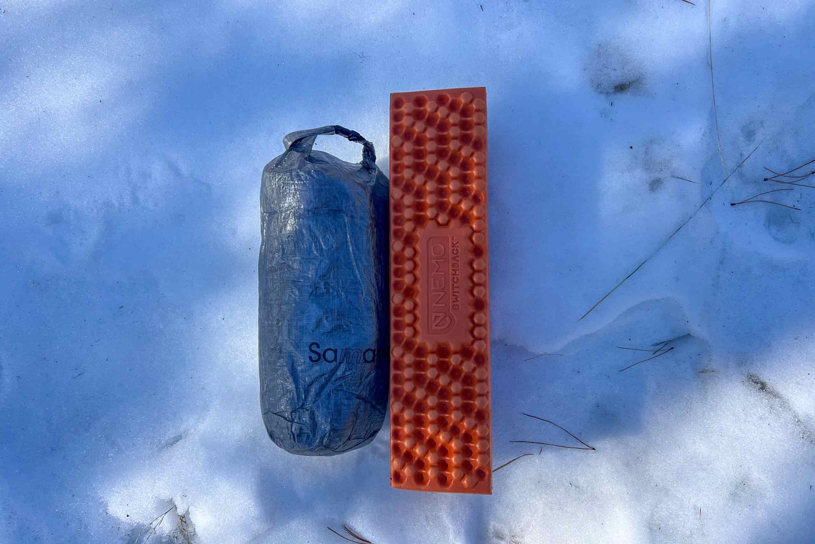 The Samaya 2.0 tent in its compact, gray storage sack placed on snow beside an orange NEMO Switchback sleeping pad.